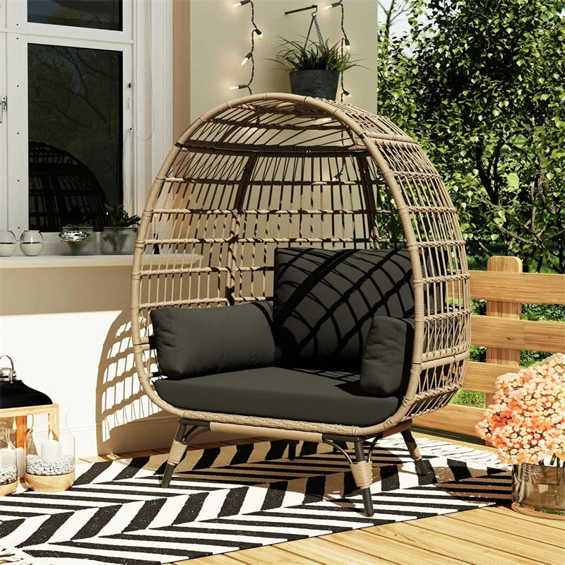 Wicker egg-shaped chair with black cushions on a patio with plants and decor.