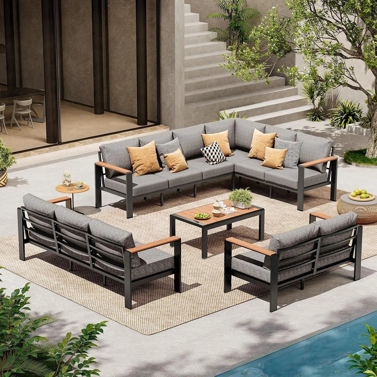 Outdoor patio furniture set with gray cushions and wooden accents on a patio with pool and stairs in the background.