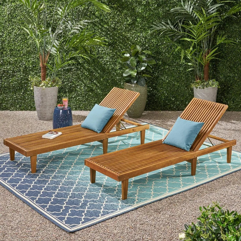 Two wooden lounge chairs with blue cushions on a patterned outdoor rug, surrounded by plants.