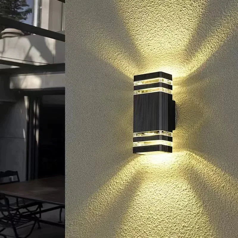 Modern outdoor wall light fixture on a textured wall with outdoor furniture in the background.