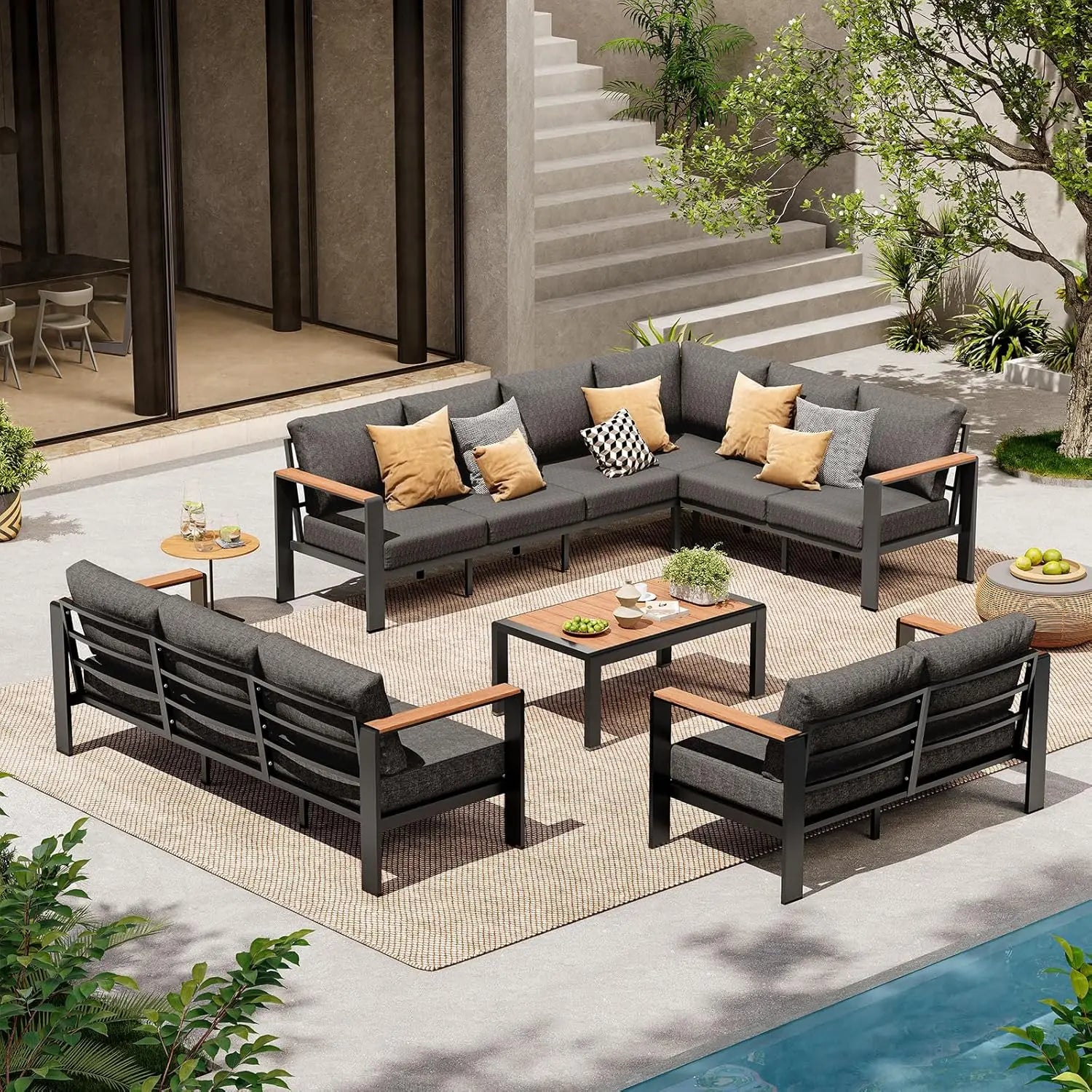 Outdoor patio furniture set with gray cushions and wooden accents on a patio with plants and a pool.