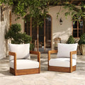 Two wooden chairs with white cushions on a stone patio