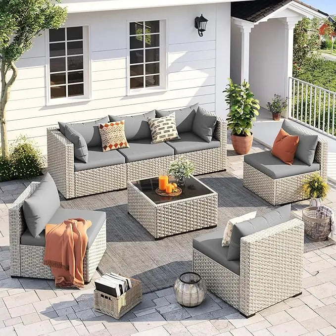 Outdoor patio furniture set with gray cushions and orange throws on a patio.