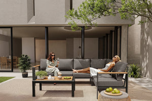 Two women relaxing on a modern outdoor sofa set with 'ComfCove' branding.