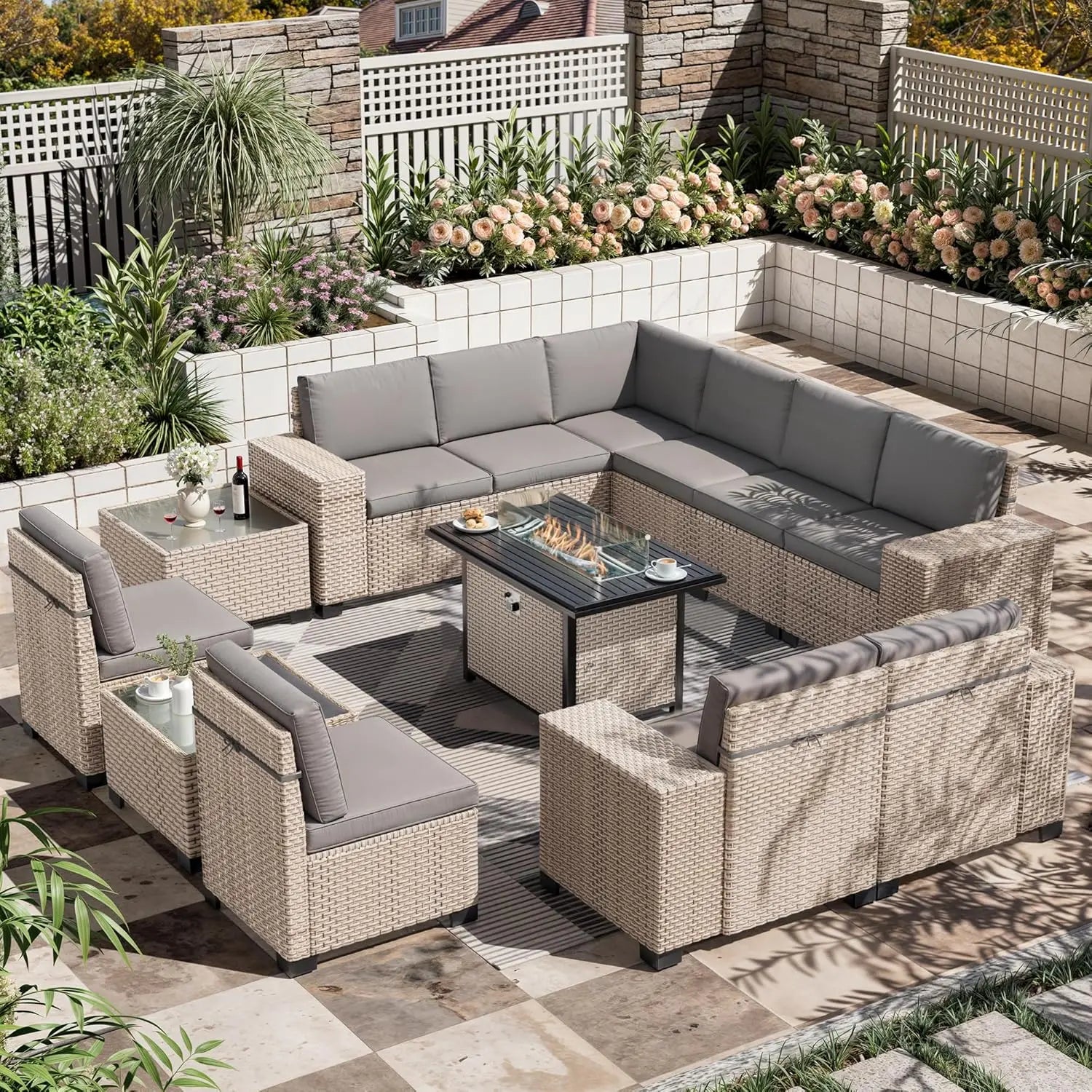 Outdoor patio furniture set with fire pit table on a patio with plants and flowers.