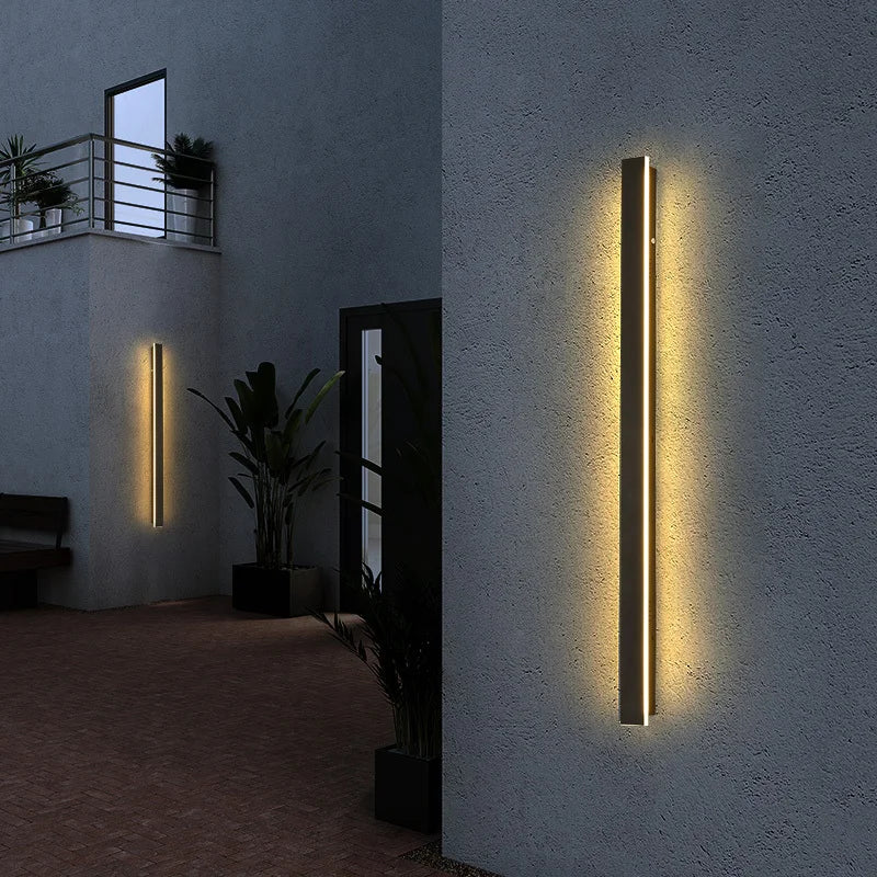 Modern outdoor wall lights on a textured wall with plants and a bench in the background.